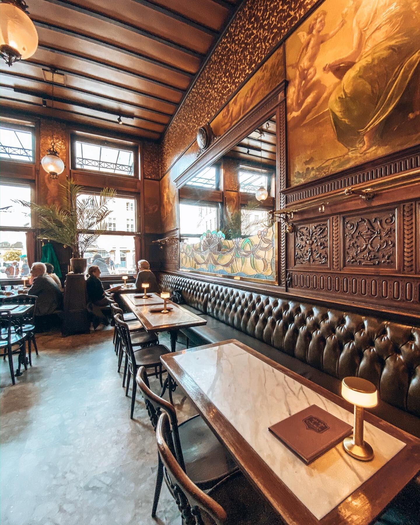 Het interieur van Brasserie Gambrinus: groene lederen banken, eiken lambrisering en een beschilderd plafond