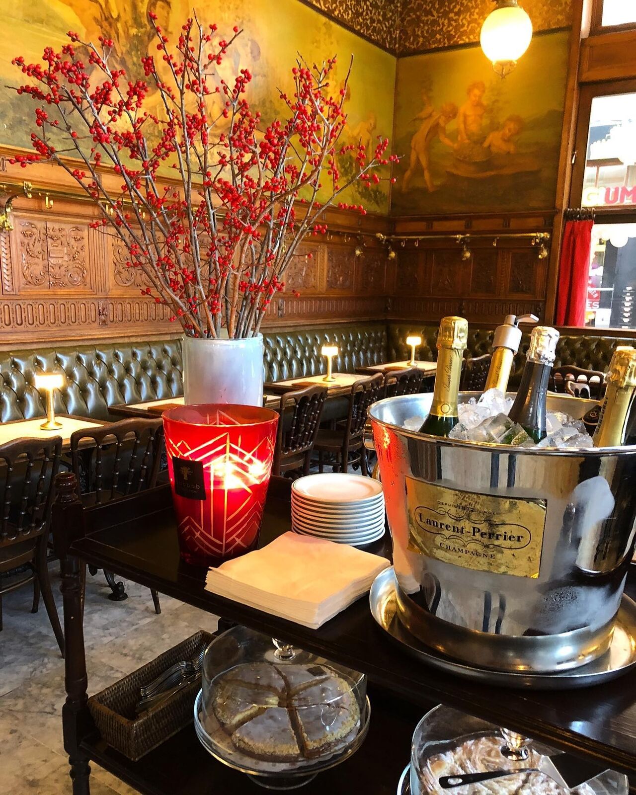 De zaal van Gambrinus met beschilderd plafond, groene lederen banken en een koelemmer met champagne